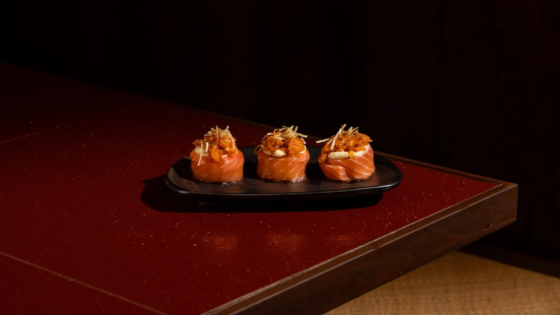 Spicy Salmon gunkan with sriracha and mentai sauce served on a dark plate at Shinraku Ubud