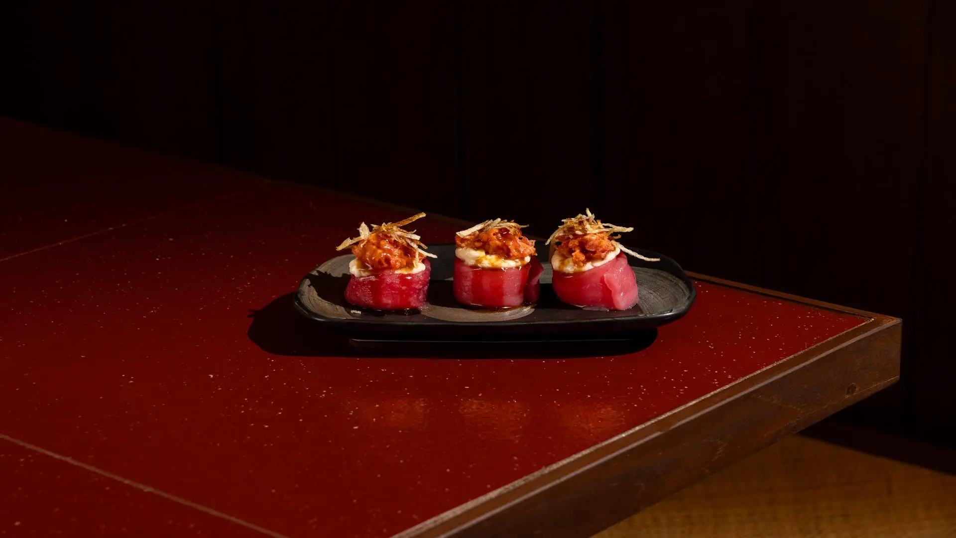 Spicy Tuna gunkan with sriracha and mentai sauce served on a dark plate at Shinraku Ubud